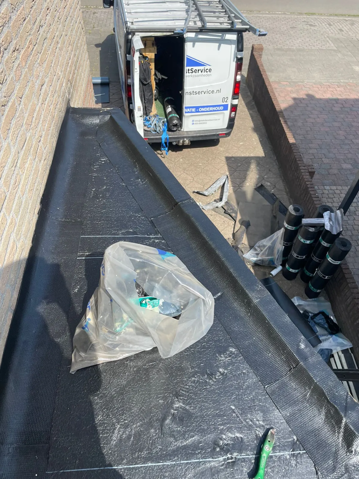 Plat dak met opstand en dakrand naast een oprit, bedrijfsbus op de achtergrond