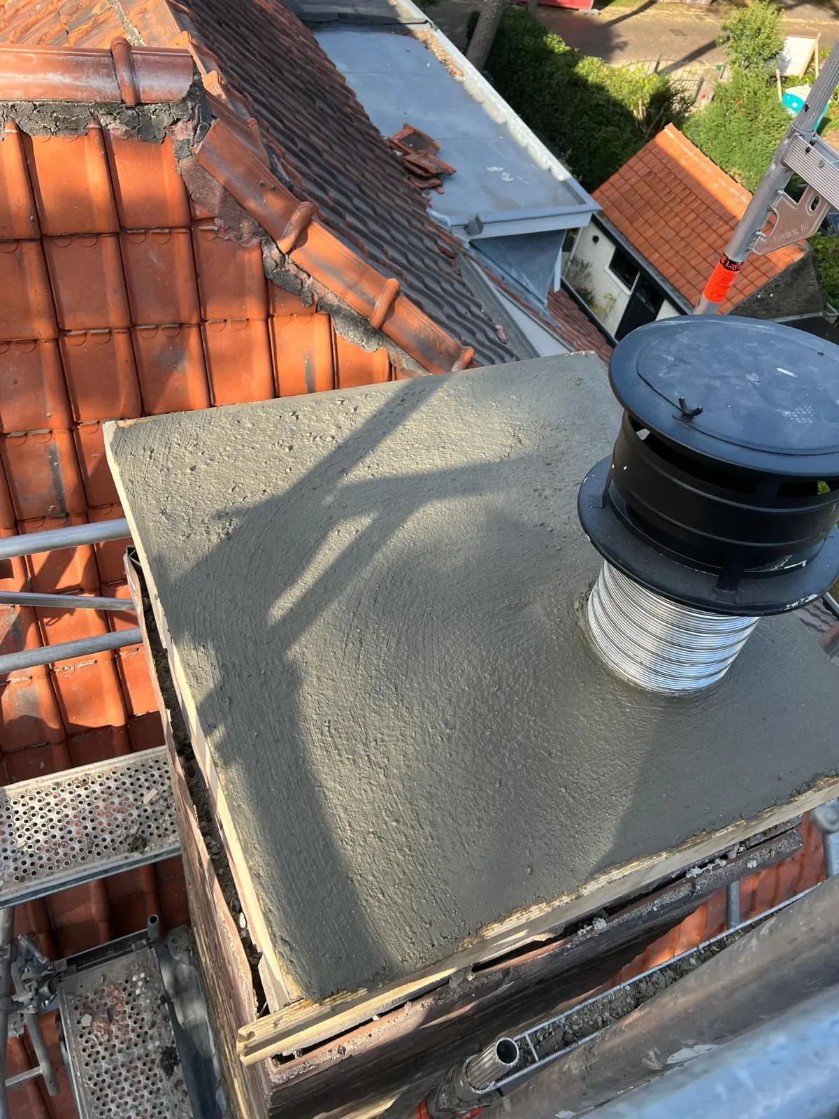 Schoorsteen met nieuwe betonnen afdekplaat en kap op een pannendak